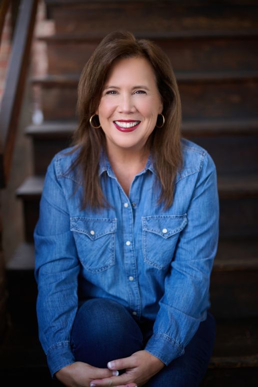 A professional head shot of Author and Essay coach Ellen Weeren in sitting on stairs.